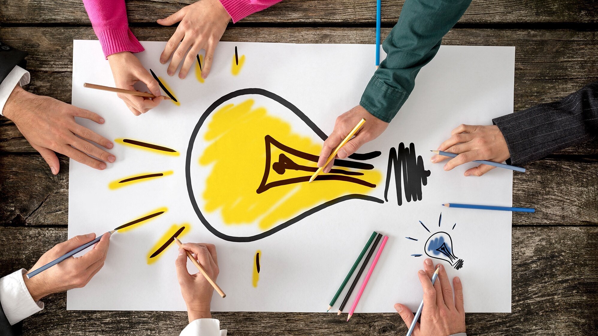 Hände von Schülerinnen und Schülern malen an einem Bild mit einer Glühbirne darauf