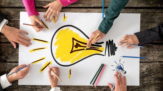 Hände mit Stiften auf einem Tisch, arbeiten an einer Zeichnung mit einer Glühbirne