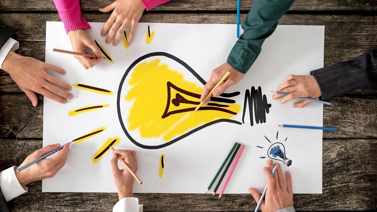 Hände, die mit Buntstiften an einem Glühbirnenbild zeichnenan einer Glühbirne