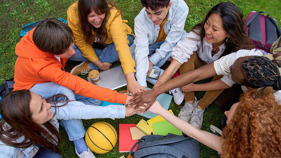 Gruppe Jugendlicher im Kreis sitzend und Hände in der Mitte aufeinandergelegt