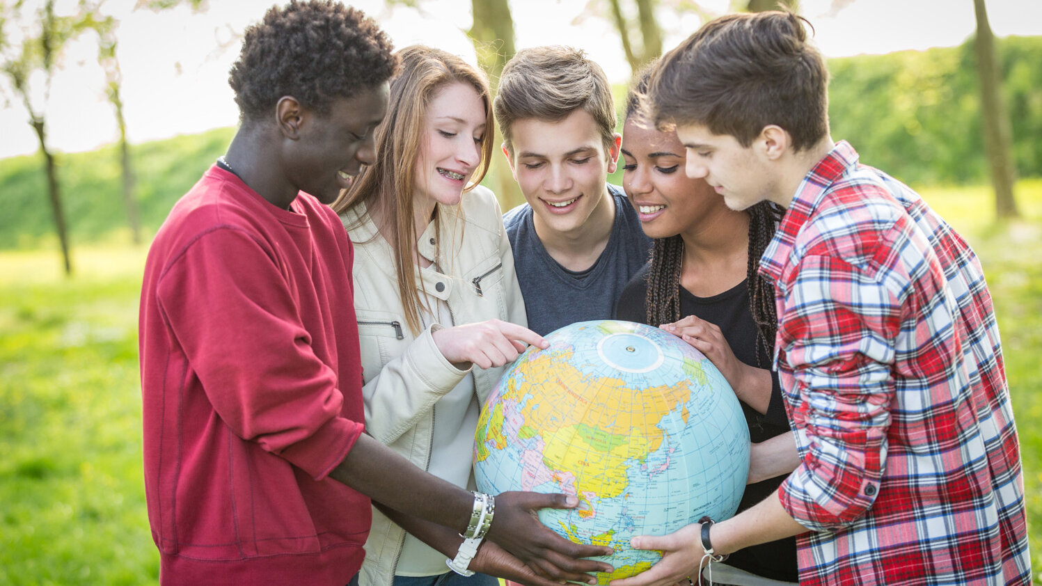 Gruppe von Schülerinnen und Schülern hält eine Weltkugel und deutet darauf.